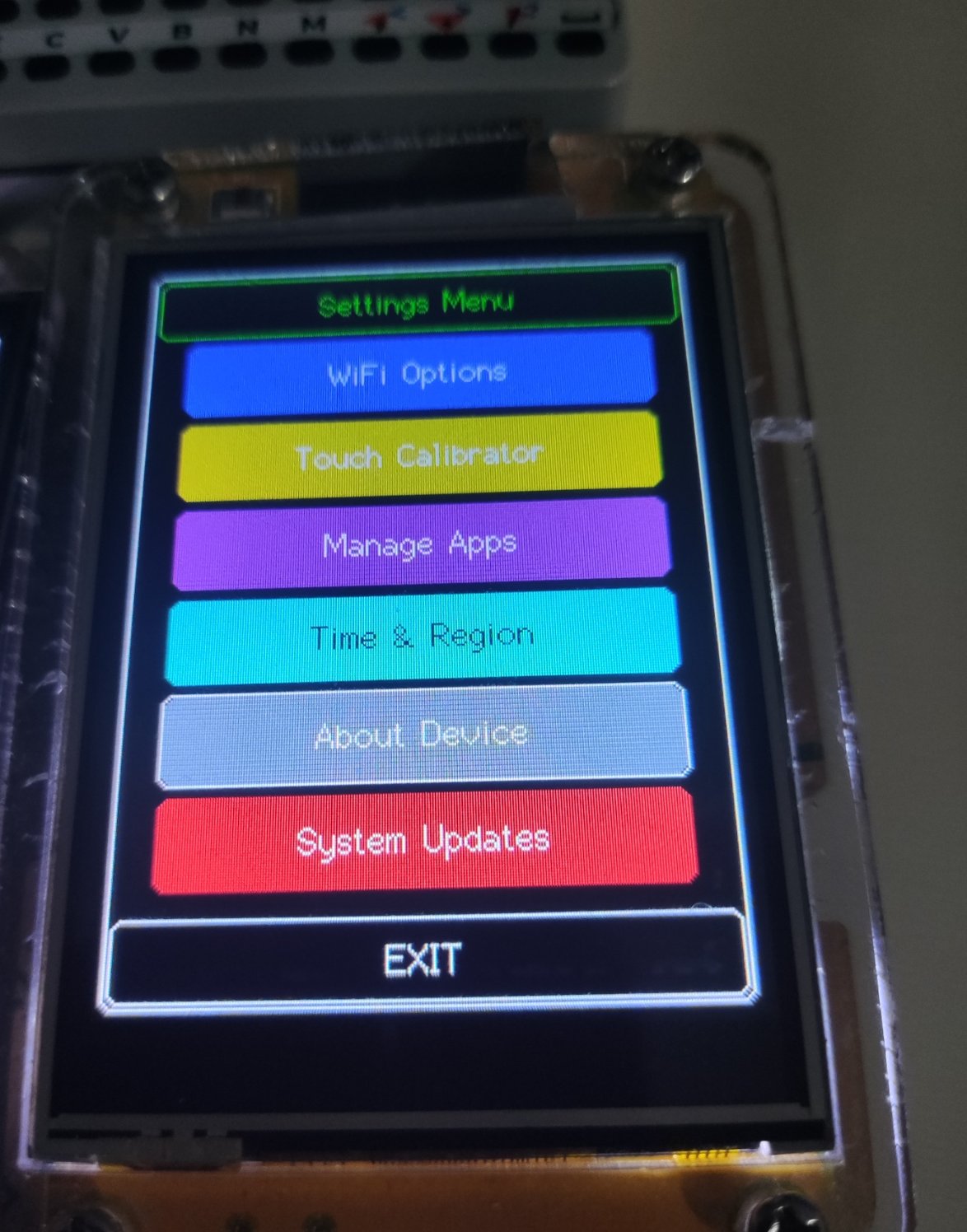 A Cheap Yellow Display in a clear case running KryonOS: the settings menu, with coloured tiles for WiFi Options, Touch Calibrator, Manage Apps, Time and Region, About Device, System Updates and EXIT.